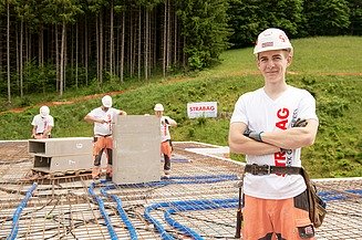 Foto eines Lehrlings mit Blick in Kamera, im Hintergrund weitere Kolleg:innen